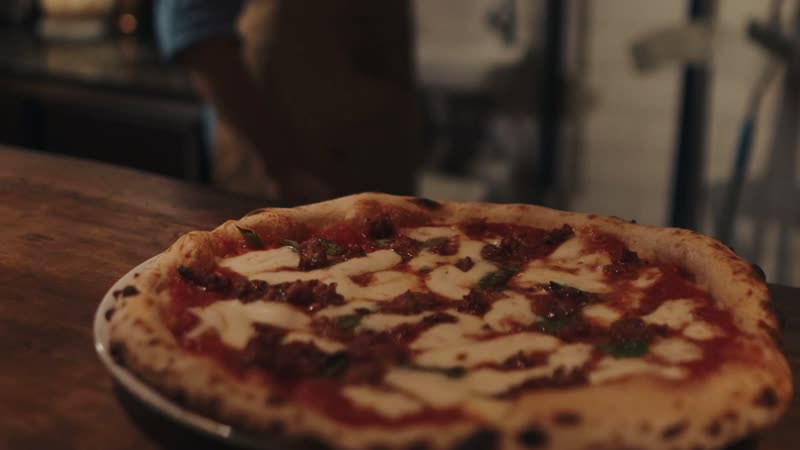 Uma margherita recém-saída do forno sobre a bancada de madeira, com a borda malhada de escuro.