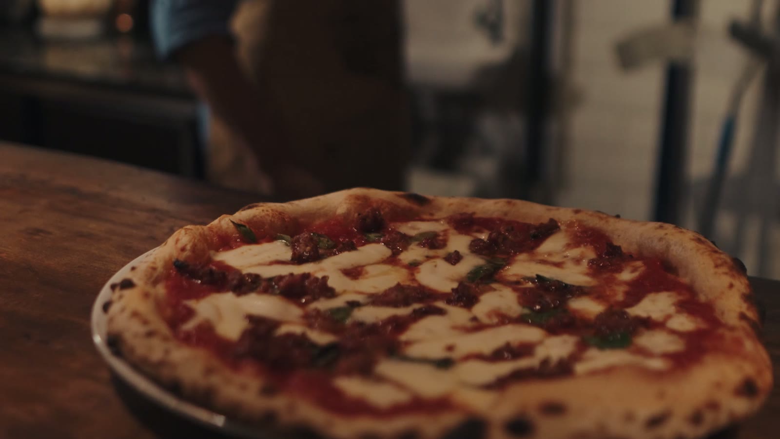 Uma margherita recém-saída do forno sobre a bancada de madeira, com a borda malhada de escuro.